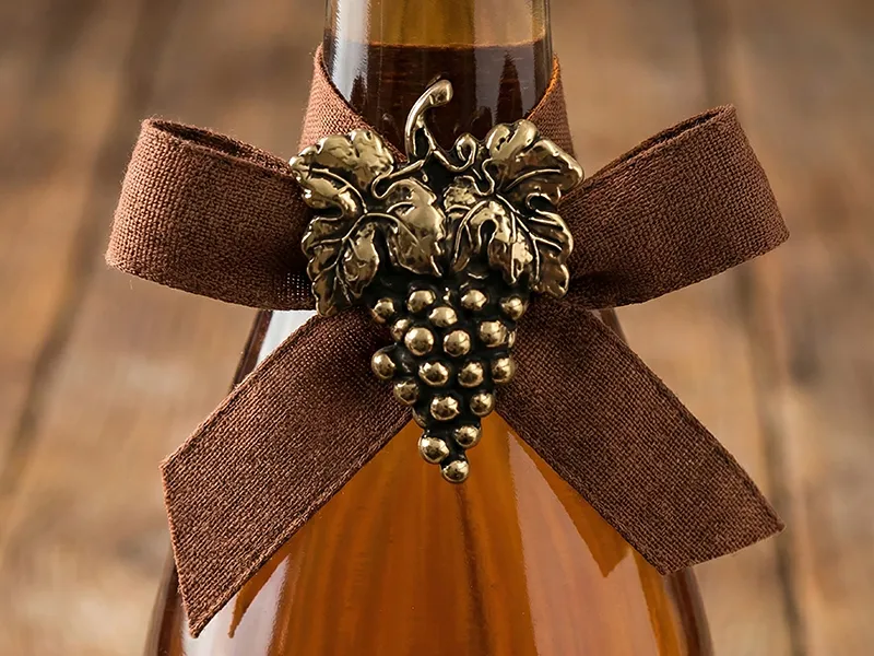 Broche decorativo de zamak con forma de racimo de uvas fijado al lazo de una botella